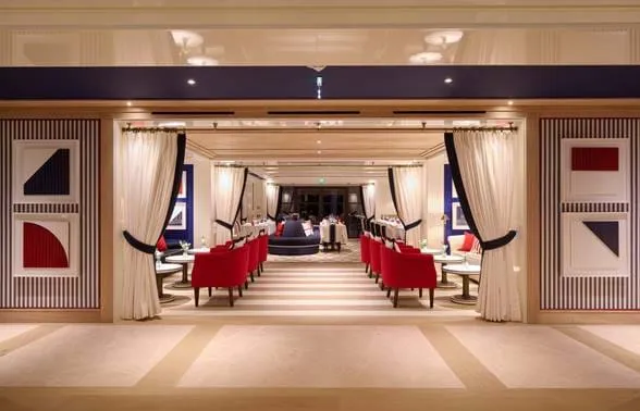 Elegante entrada do restaurante do hotel AREV em Saint-Tropez, com cortinas brancas e poltronas de veludo vermelho.