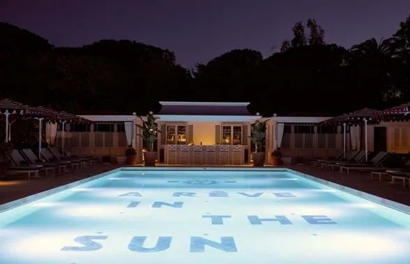 Vista nocturna da piscina iluminada do hotel AREV Saint-Tropez, com a inscrição “A Rève In The Sun” no piso da piscina.