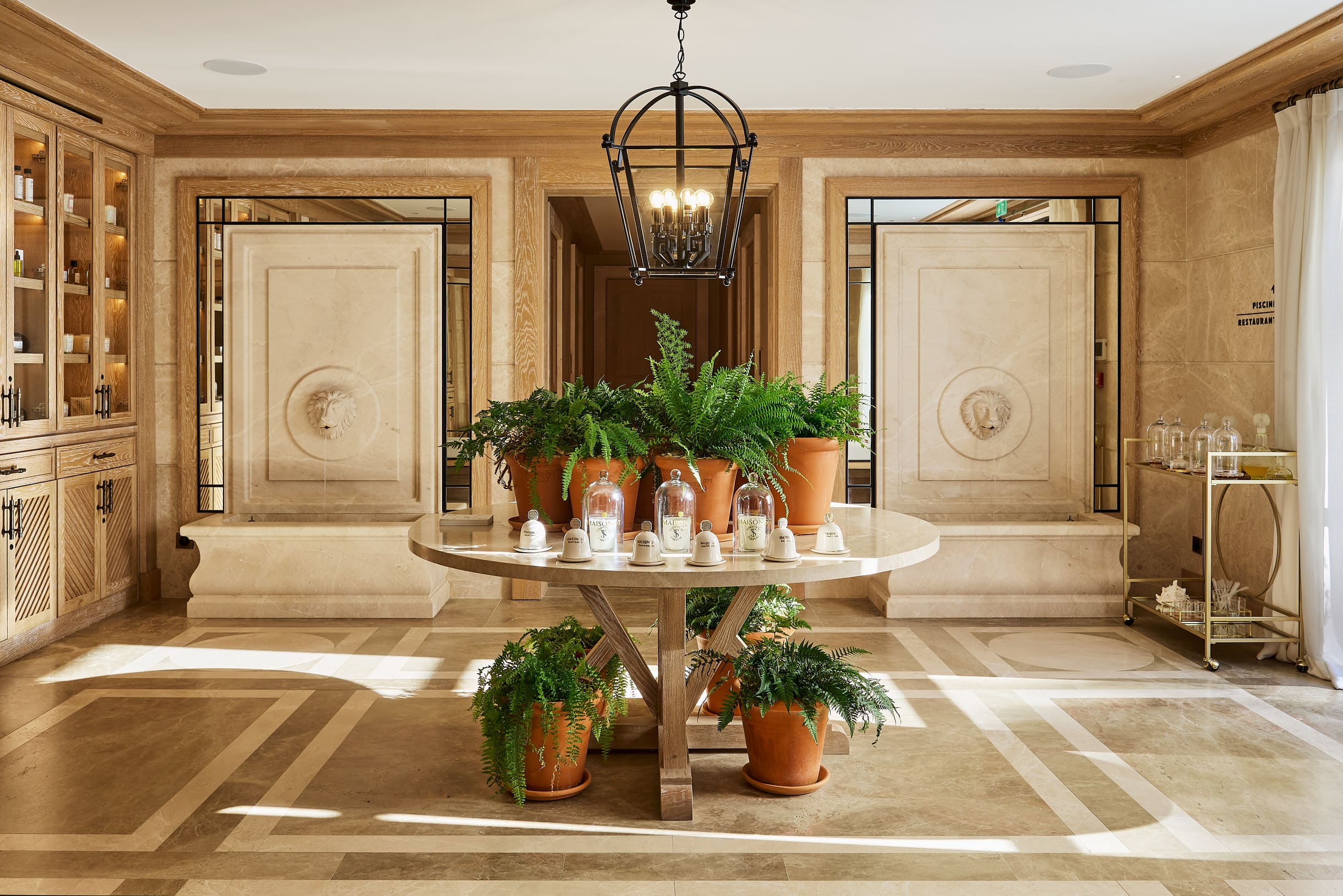Elegante quarto com uma mesa redonda de madeira com lavabaias em vasos e velas perfumadas, ladeado por fontes de parede de pedra com face de leão e armários de madeira.