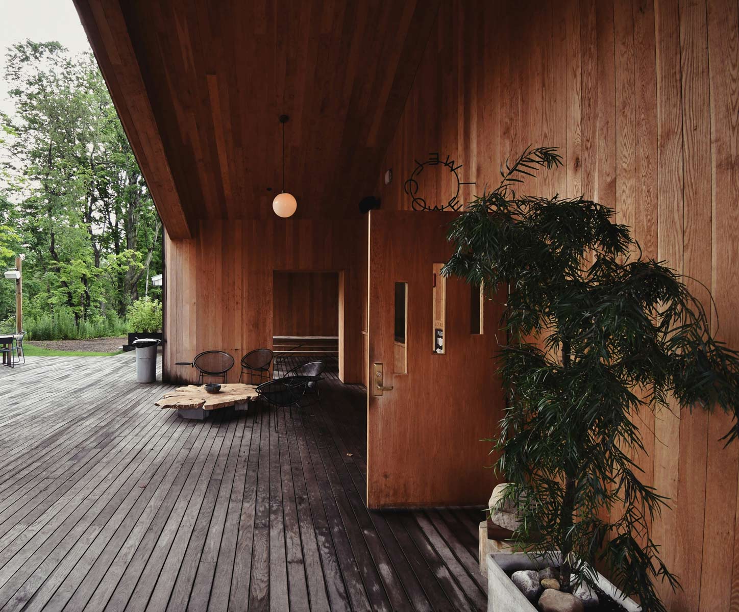 Überdachte Holzterrasse mit moderner Sitzecke aus schwarzem Metall, rustikalem Holztisch und großer Topfpflanze.