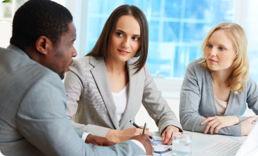 Three diverse business professionals having a focused discussion around a table with documents and glasses of water.