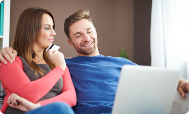 Smiling couple sitting on a couch, using a laptop with a credit card in hand.