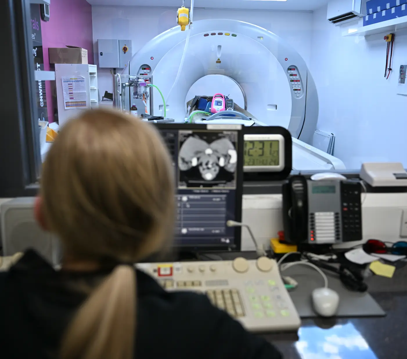 Technician monitoring a CT scan procedure on a computer screen in a medical imaging room.