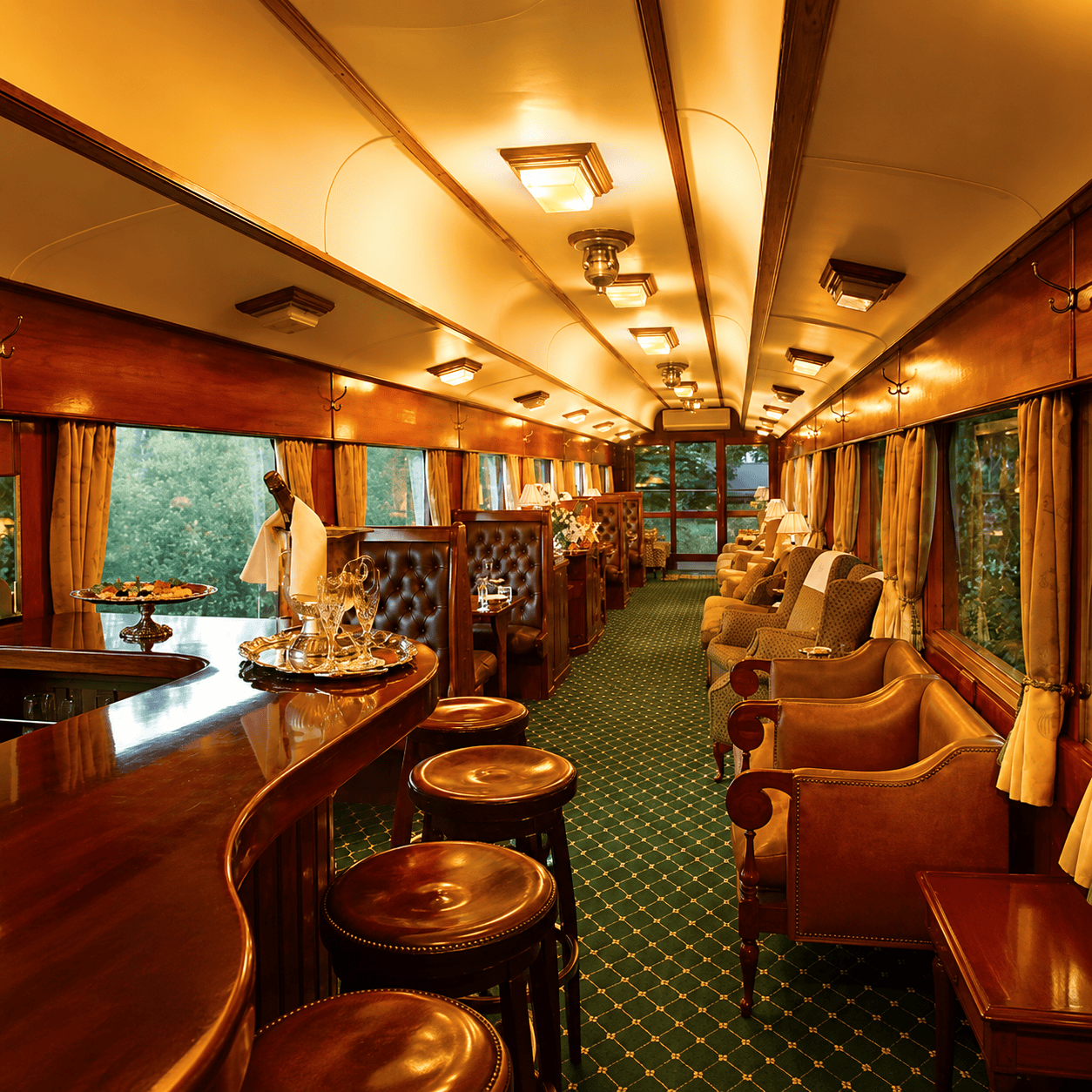 A blue and white luxury train travels through a vast, golden high-altitude plain next to a large lake under a cloudy sky.
