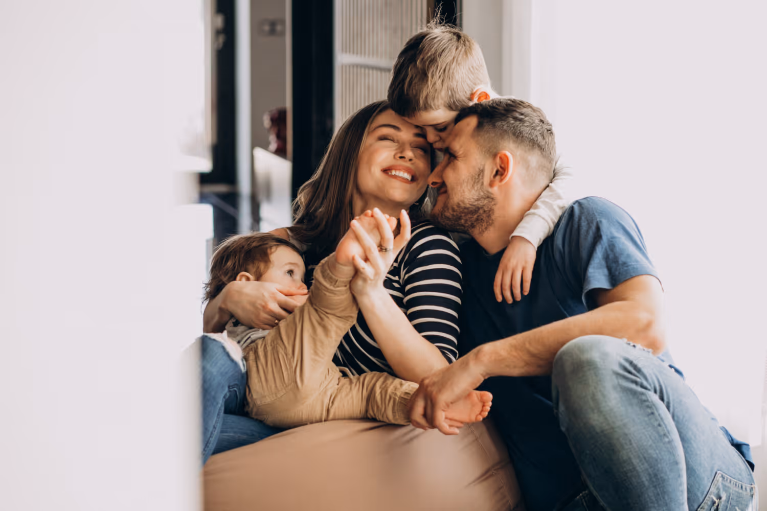 Smiling family of four sitting closely, with children embracing parents affectionately.