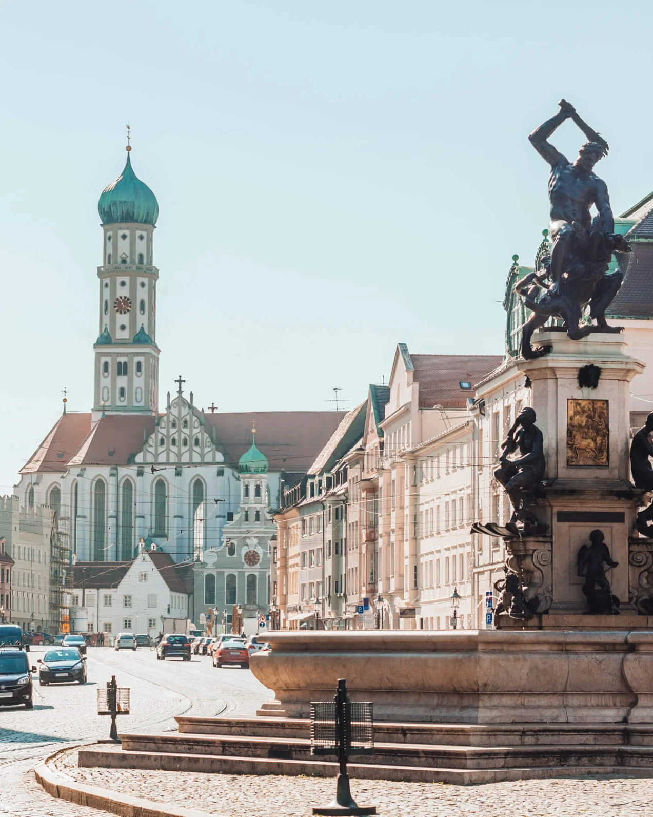 Historischer Kirchenturm und Statue auf einem Brunnen in einer belebten deutschen Stadt.