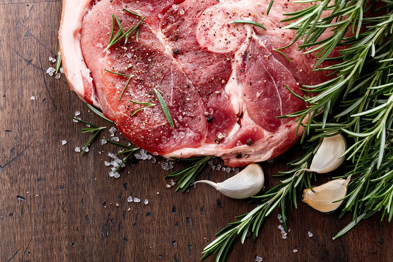 Roher, mariniertet Rindersteak mit Rosmarin, Knoblauch und grobem Salz auf Holzbrett.
