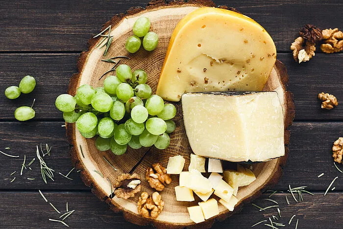 Käsescheiben und -würfel mit grünen Trauben und Walnüssen auf Holzbrett.