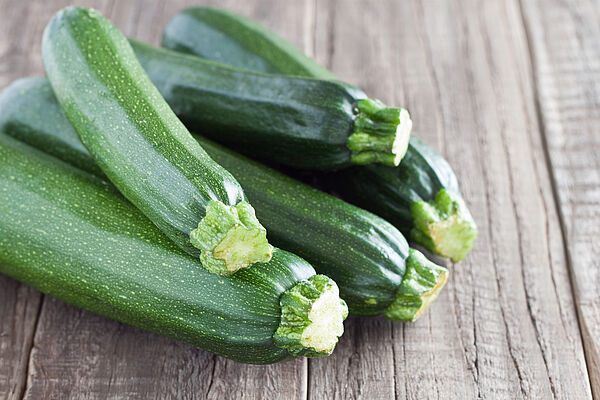 Fünf frische grüne Zucchini liegen auf einem hölzernen Tisch.