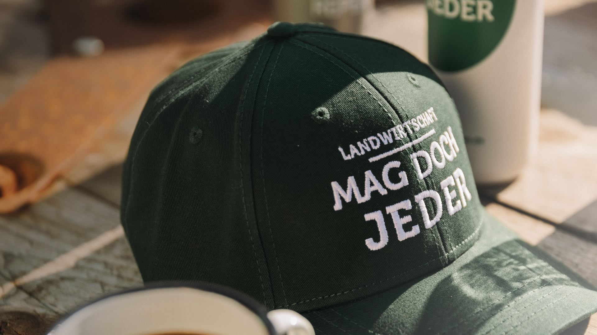 Grüner Baseball-Cap mit weißer Aufschrift Landwirtschaft mag doch jeder auf Holztisch.