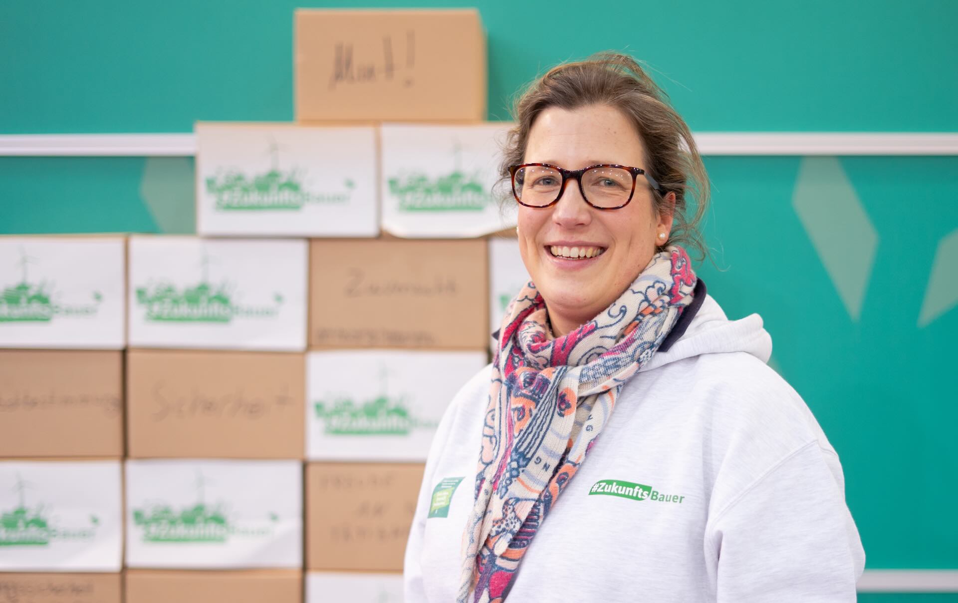 Eine Frau die in die Kamera lächelt, im Hintergrund ist eine Messewand zu sehen.