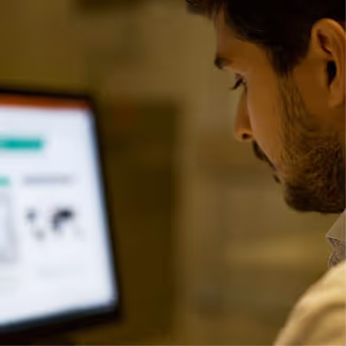 Uomo con barba che guarda uno schermo di computer sfocato.