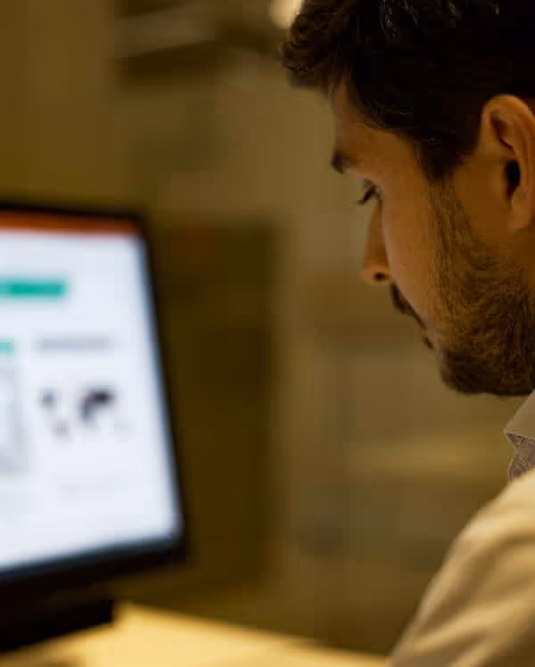 Uomo con barba che guarda uno schermo di computer sfocato in un ambiente interno.