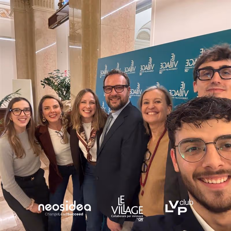 Uomo che presenta con microfono davanti a un pubblico seduto in una sala conferenze moderna con schermo digitale sullo sfondo.