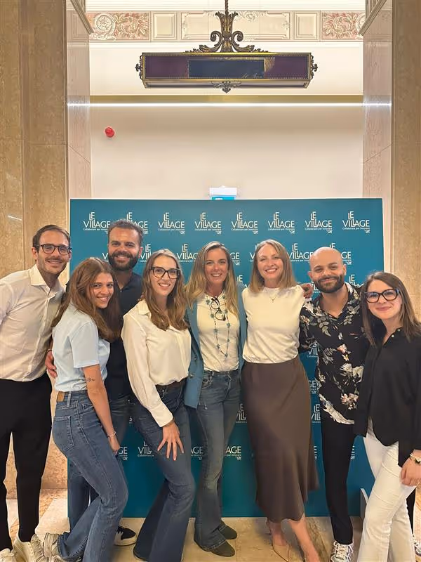 Uomo che presenta con microfono davanti a un pubblico seduto in una sala conferenze moderna con schermo digitale sullo sfondo.