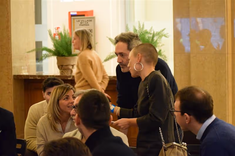 Gruppo di persone in un ambiente interno che chiacchierano tra loro durante un incontro sociale.