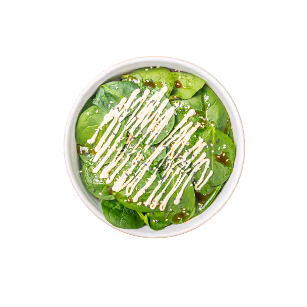 Eine weiße Schüssel gefüllt mit frischen Spinatblättern, beträufelt mit cremiger Soße und bestreut mit Sesamkörnern, vor schwarzem Hintergrund.