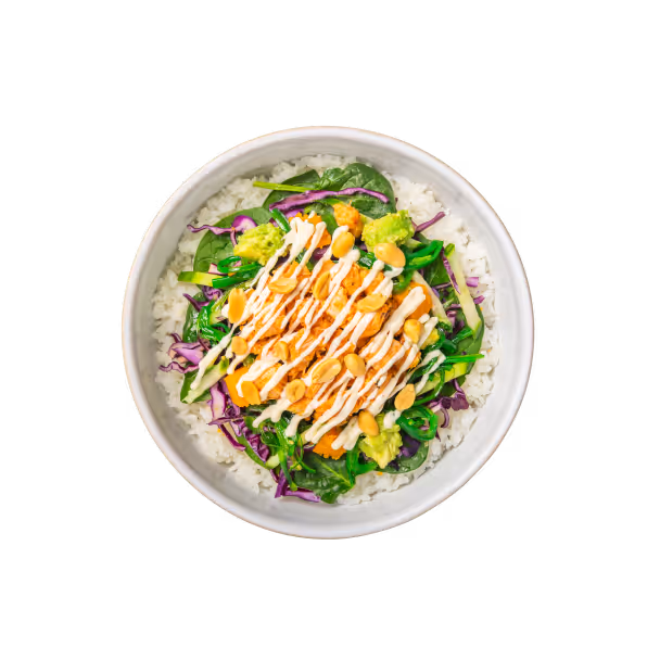 Eine farbenfrohe Schüssel Reis mit gemischtem Blattgemüse, gewürfelter Avocado, geraspelten Karotten, Rotkohl, beträufelt mit cremigem Dressing und bestreut mit Erdnüssen.