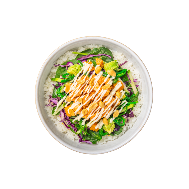 Eine farbenfrohe Schüssel Reis mit gemischtem Blattgemüse, gewürfelter Avocado, geraspelten Karotten, Rotkohl, beträufelt mit cremigem Dressing und bestreut mit Erdnüssen.