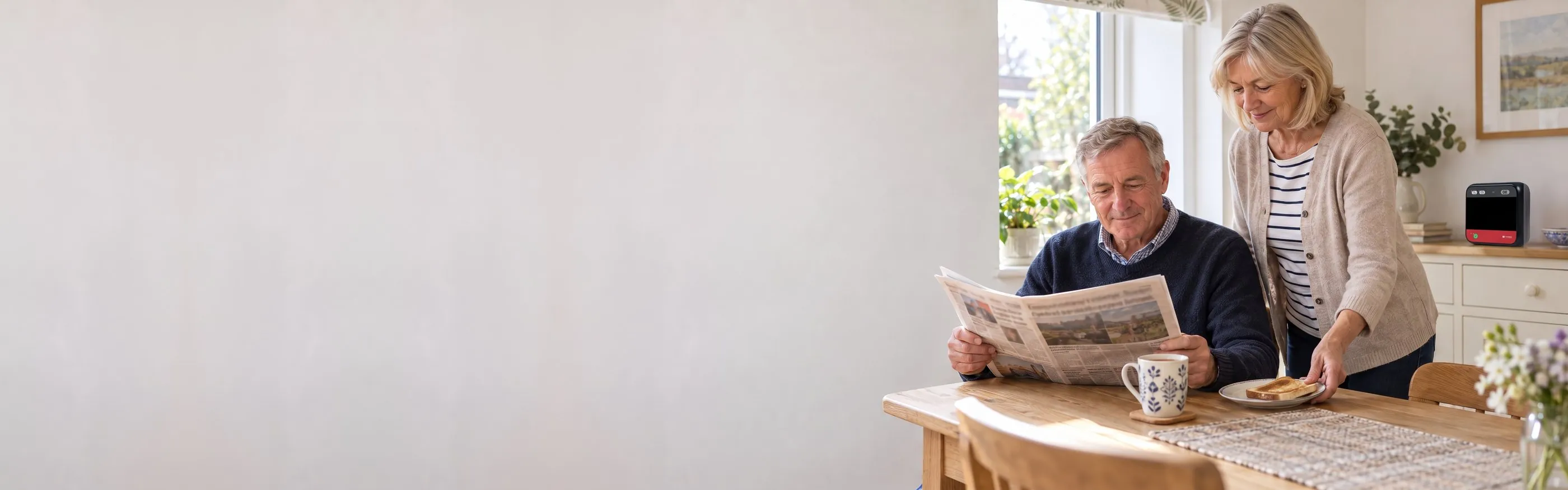 An older couple having breakfast at home, with their home defibrillator on the dresser behind them