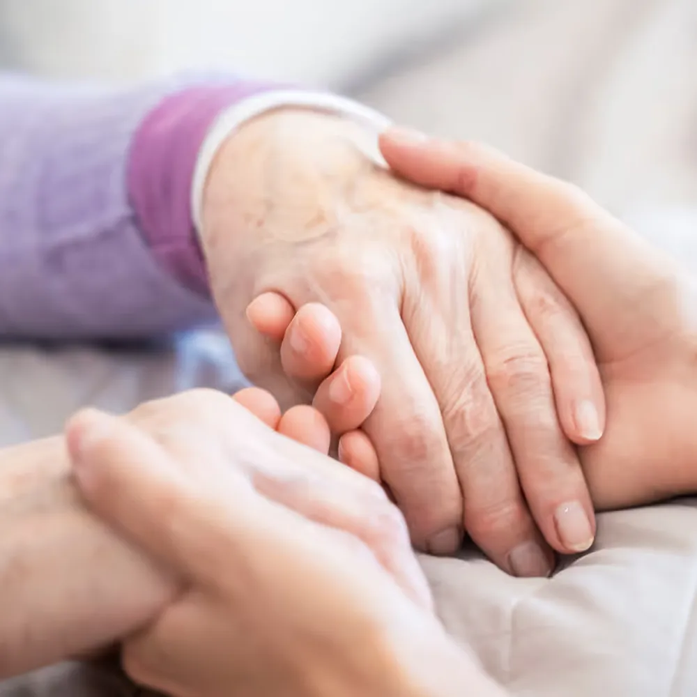 Zwei Hände halten liebevoll eine ältere Hand als Zeichen von Fürsorge und Unterstützung.