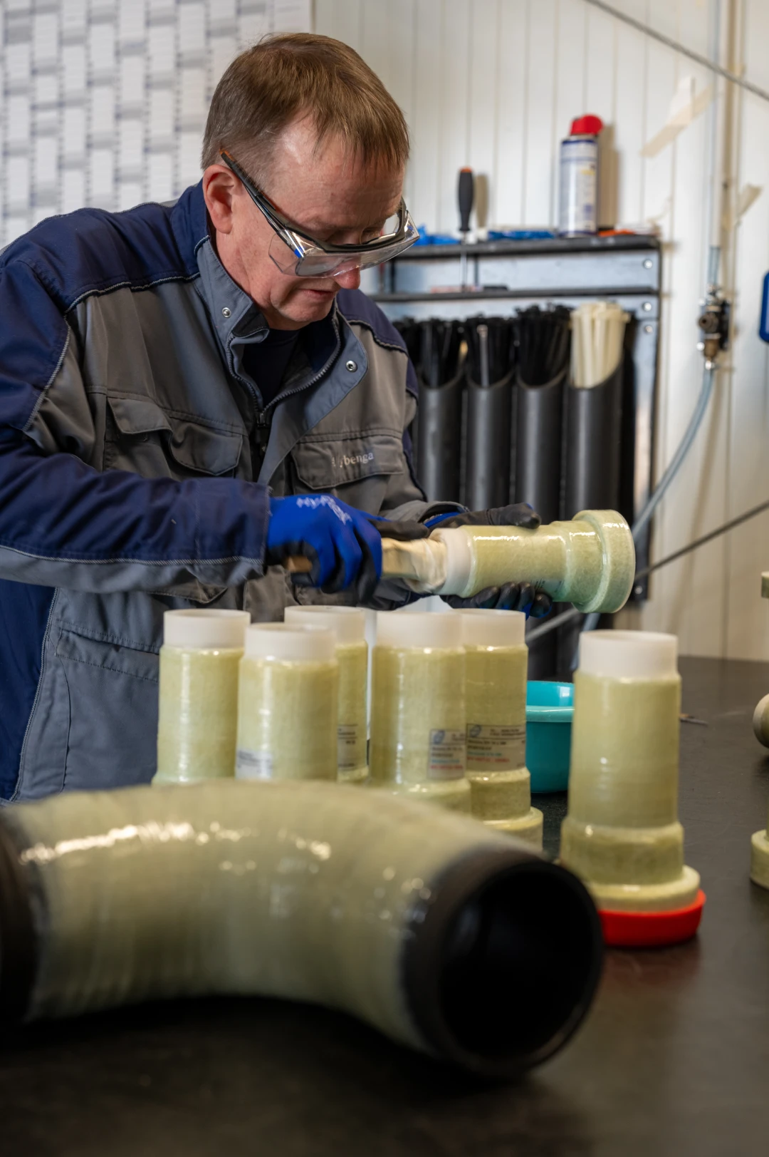 Mitarbeiter mit Schutzbrille und Handschuhen arbeitet an einem Fertigungsprozess mit Kunststoffrohren in der Werkstatt.