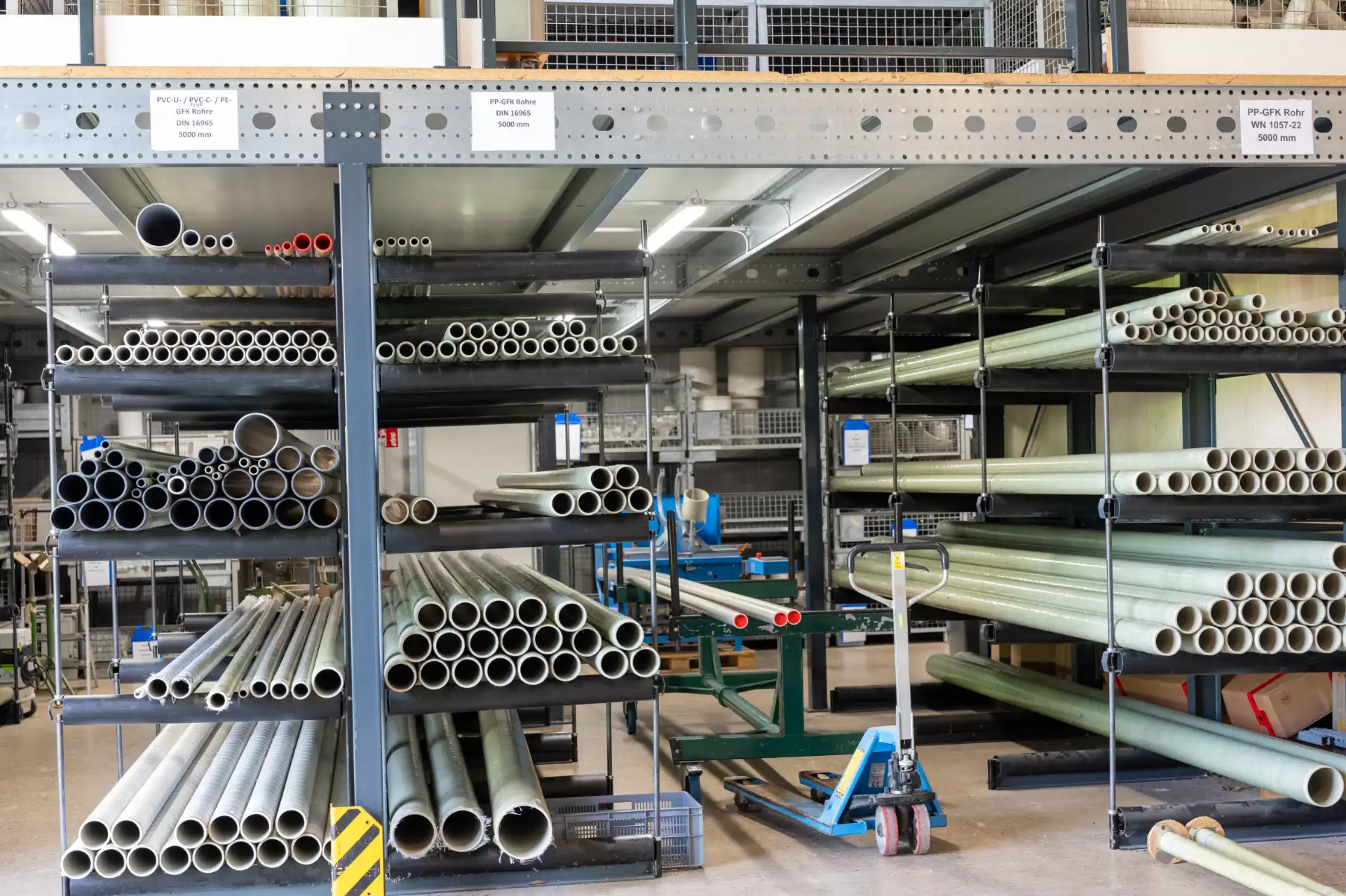 Lagerregale mit verschiedenen Kunststoffrohren, darunter PVC-, PP- und GFK-Rohre im Lagerraum.