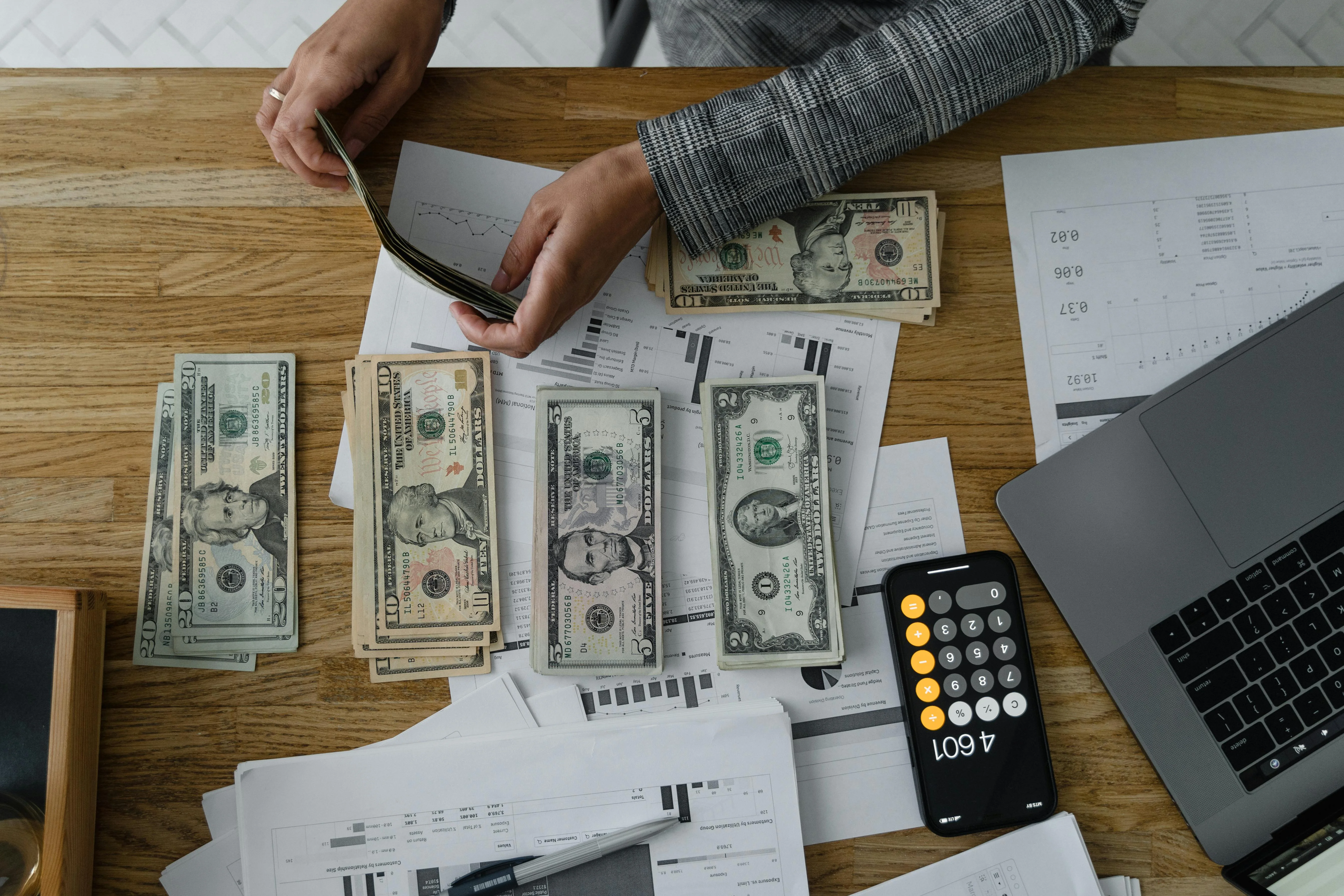 Personne comptant des billets, entourée de documents financiers, illustrant le report d'imposition sur les plus-values.