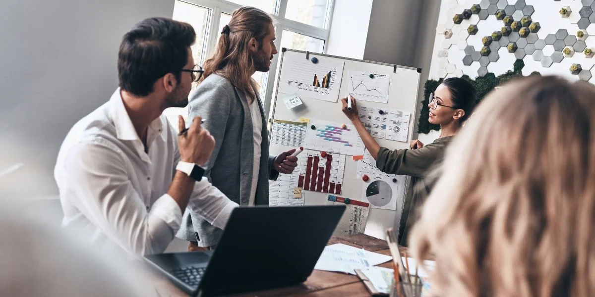 Un groupe de professionnels discute autour d'un tableau blanc rempli de graphiques et de données, illustrant les différents types de startups dans lesquelles investir pour maximiser le potentiel de rendement.