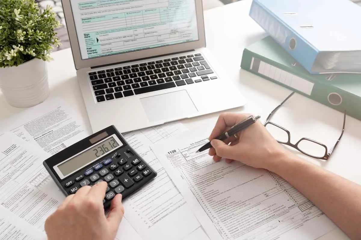 personne avec son ordinateur, un formulaire et une calculatrice pour calculer la flat tax