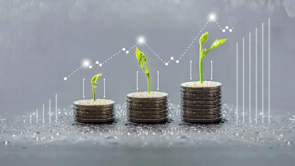 Trois piles de pièces de monnaie avec des jeunes pousses de plantes qui y poussent, illustrant la croissance et les rendements financiers grâce à l'investissement durable.