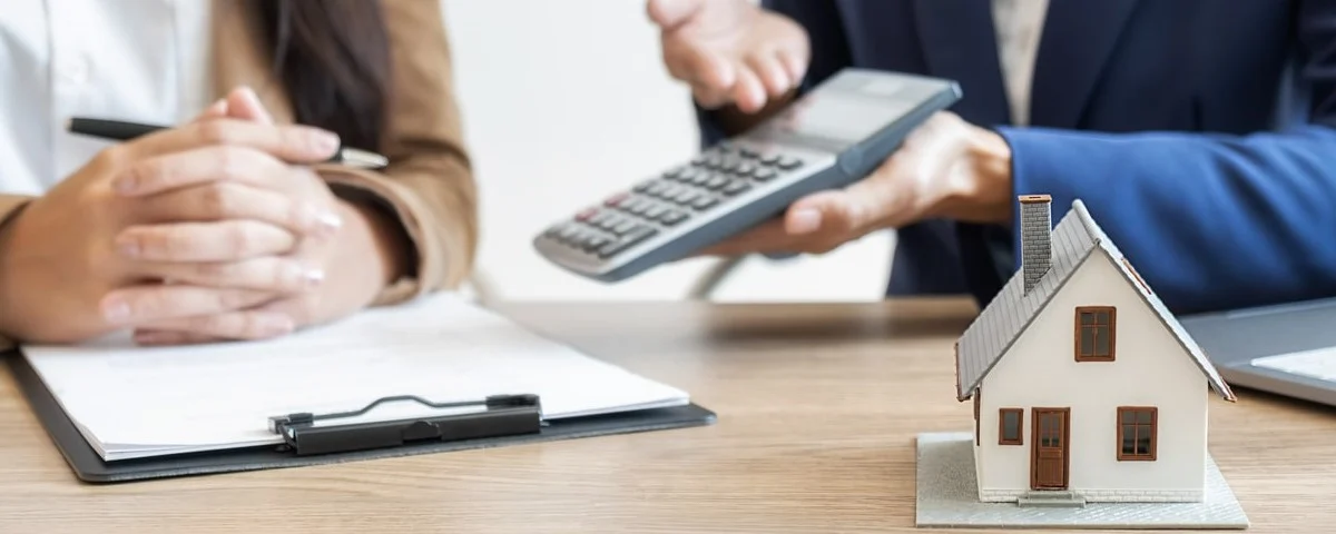 Photo d'une maquette de maison avec des gens et une calculatrice évoque un placement immobilier.
