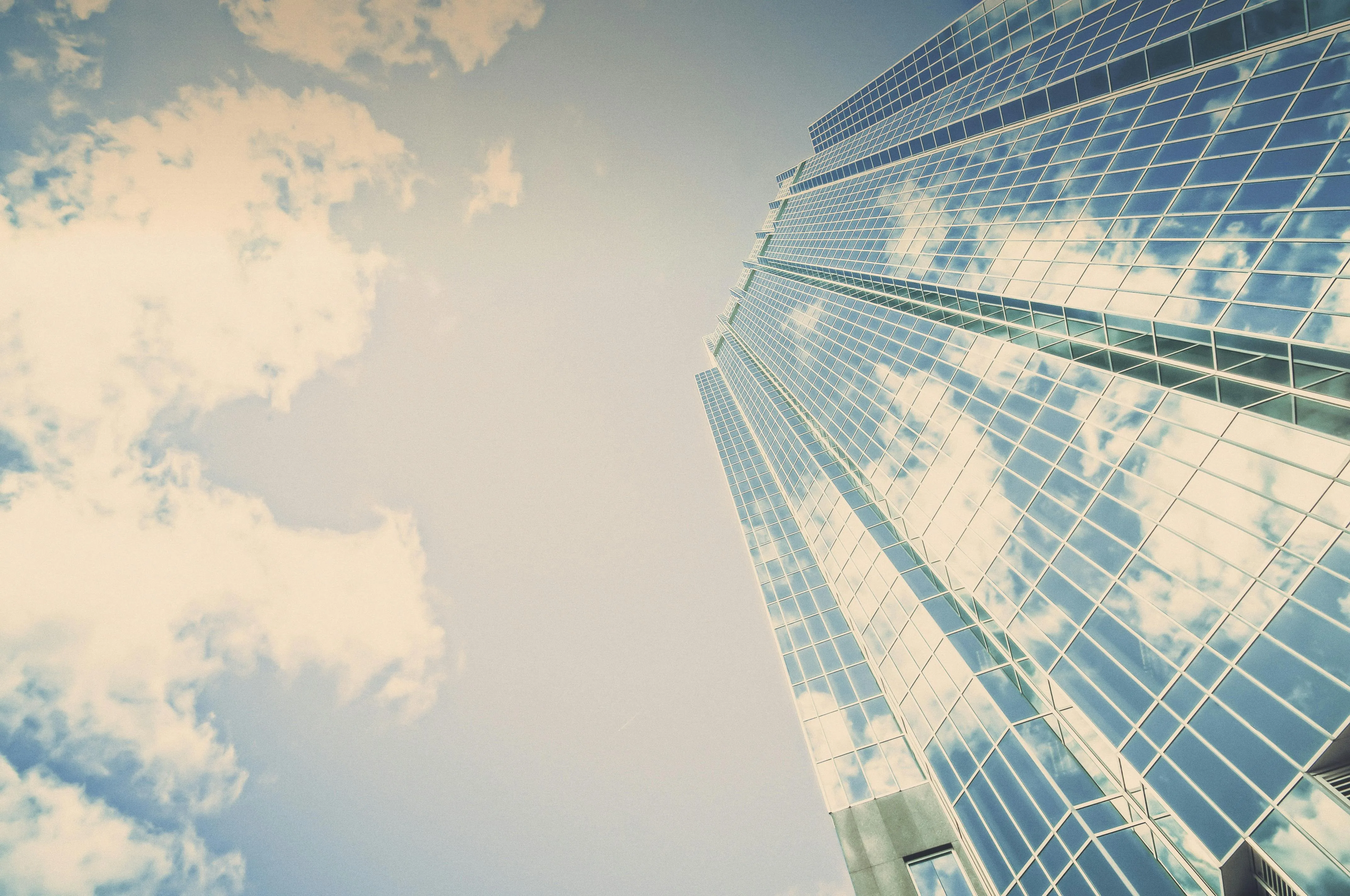 Gratte-ciel moderne avec façade vitrée reflétant le ciel et les nuages, symbolisant la structure d'une holding et l'optimisation financière grâce au report d'imposition.