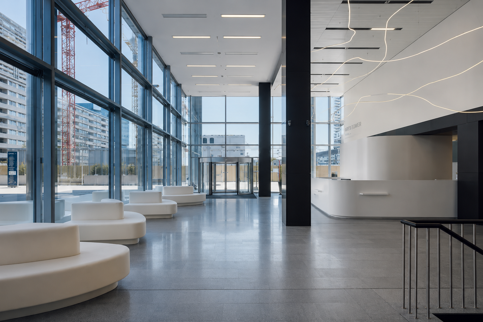 Bright modern lobby with large floor-to-ceiling windows, white curved seating, black columns, and a revolving door at the entrance.