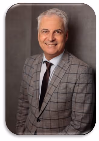 Smiling middle-aged man with gray hair wearing a gray checked suit, white shirt, and dark tie against a gray background.