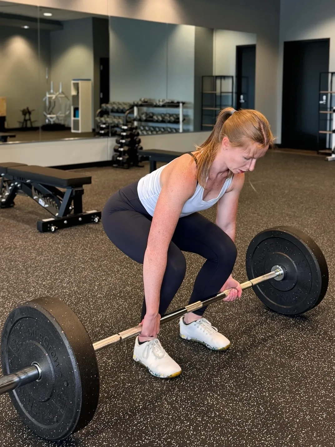 Woman in gym preparing to lift a barbell with weights from the floor.
