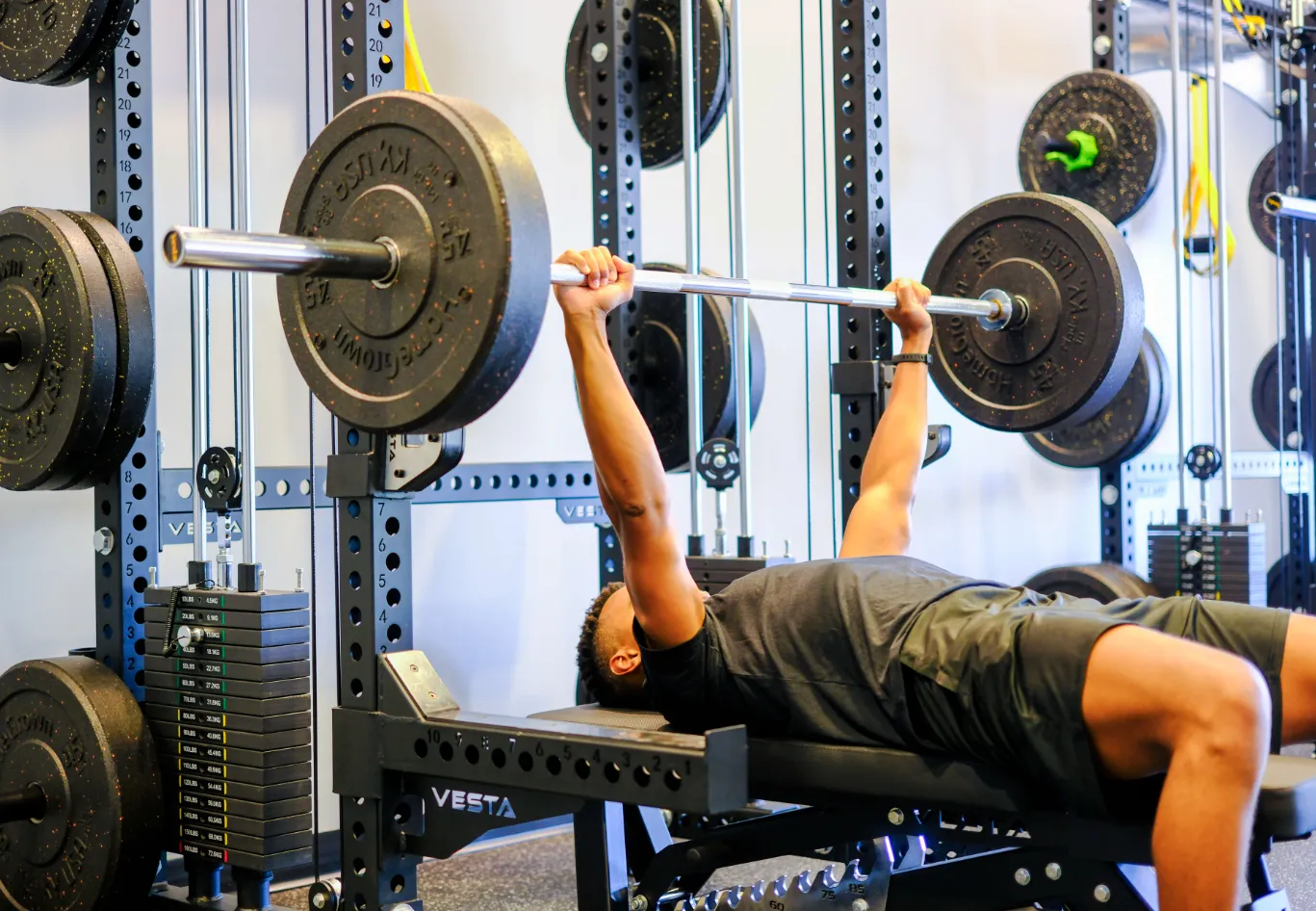 Person performing a barbell bench press in a gym with weightlifting equipment around.