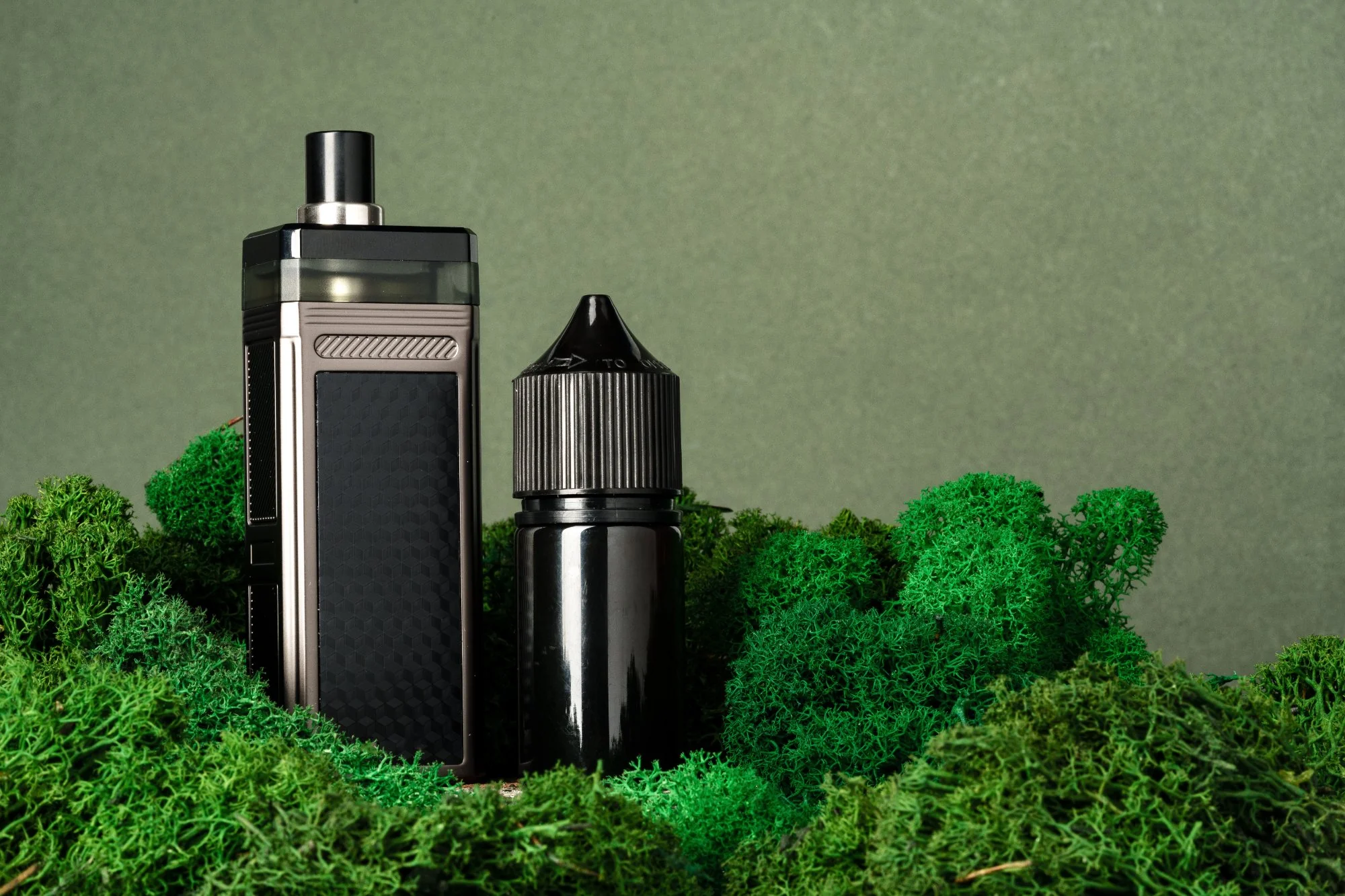 A vape mod device and e-liquid bottle placed on green moss, illustrating vaping products subject to UK WEEE compliance regulations