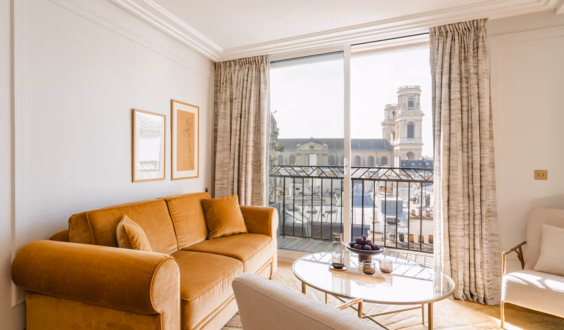 Salon lumineux avec canapé marron, table basse ronde en verre et grandes fenêtres donnant sur un bâtiment historique. - Hôtel Madison