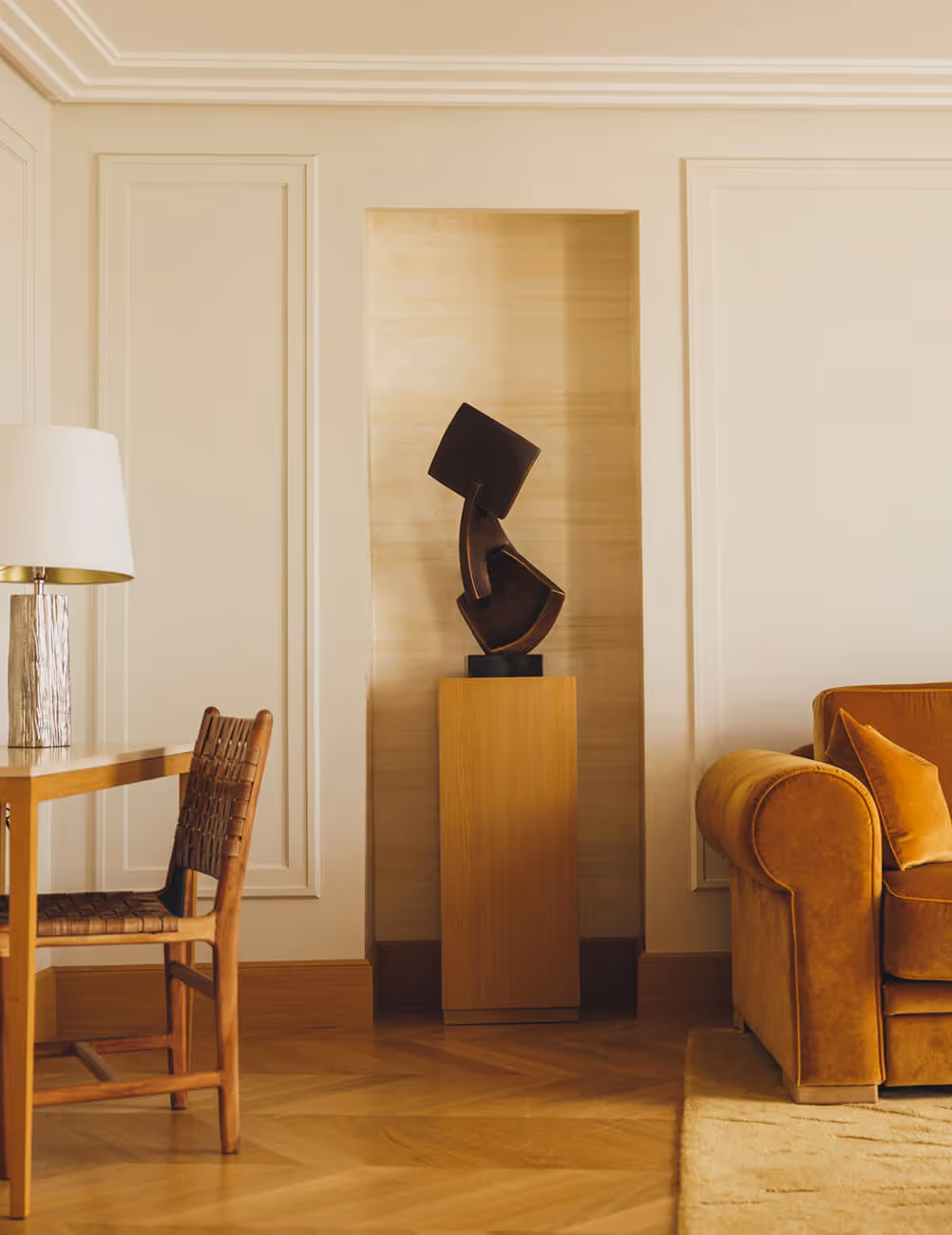 Intérieur de salon avec un canapé marron, une chaise en bois autour d'une table et une sculpture moderne noire sur un socle en bois. - Hôtel Madison