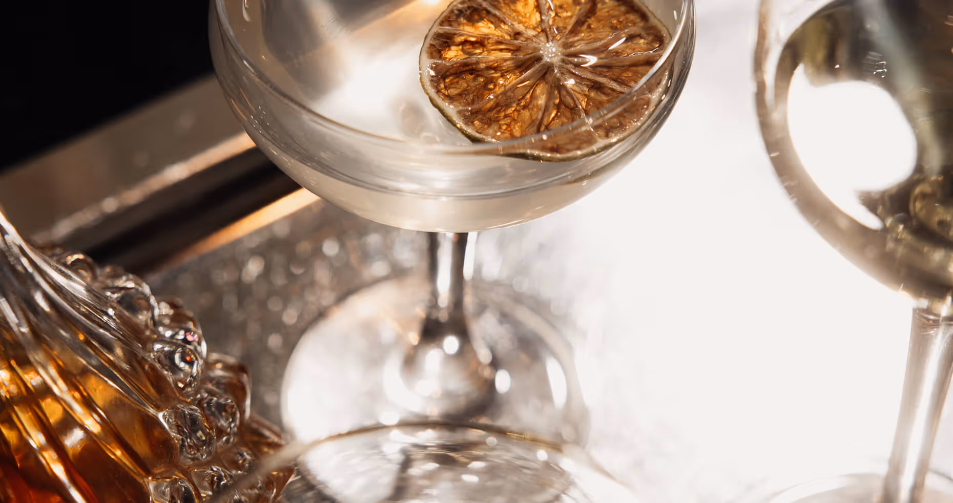 Verre à cocktail transparent avec une tranche de citron séché flottant sur la surface, posé à côté d’un verre de whisky. - Hôtel Madison