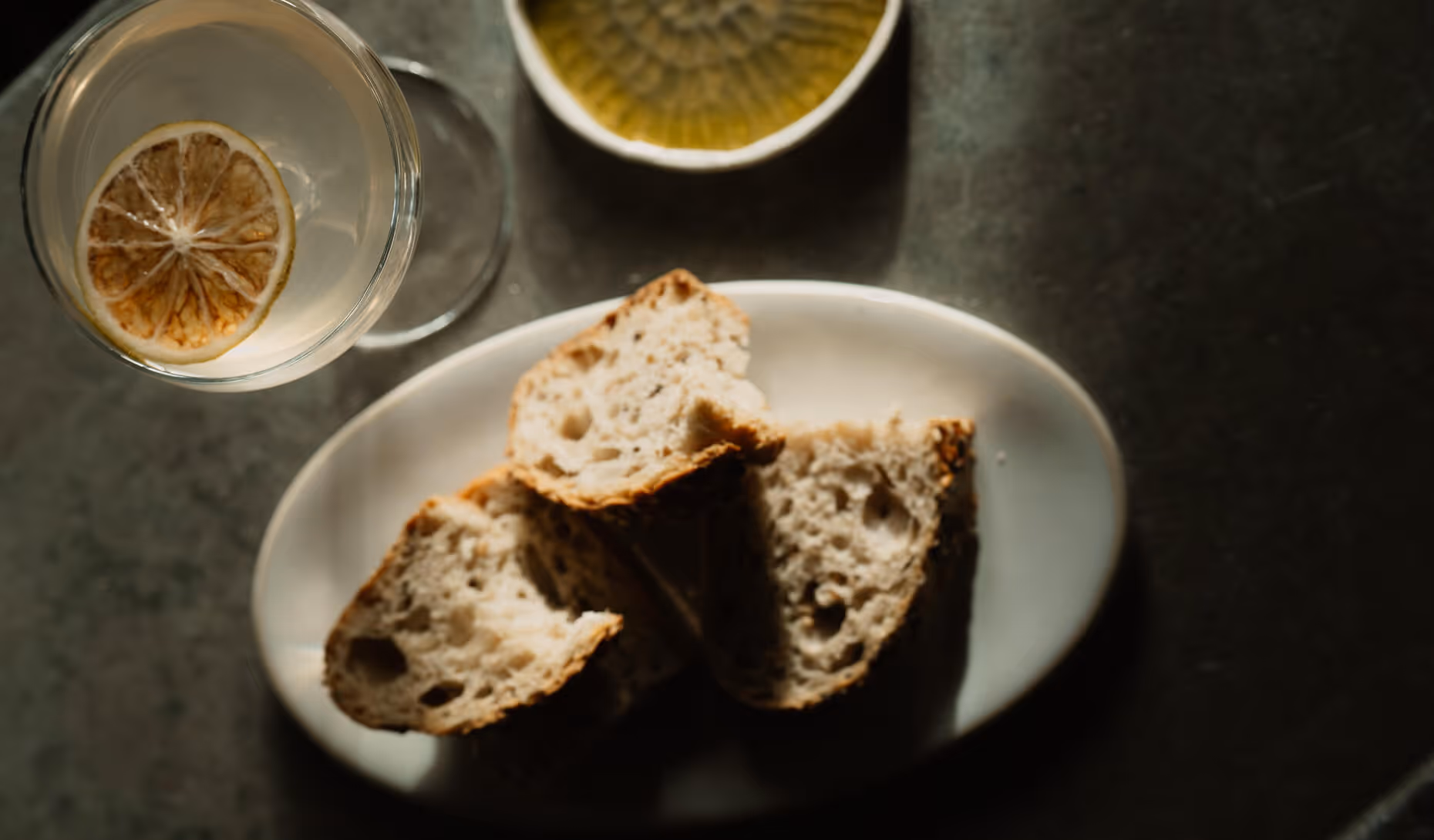 Trois morceaux de pain artisanal sur une assiette blanche, accompagnés d'un verre d'eau avec une tranche de citron. - Hôtel Madison