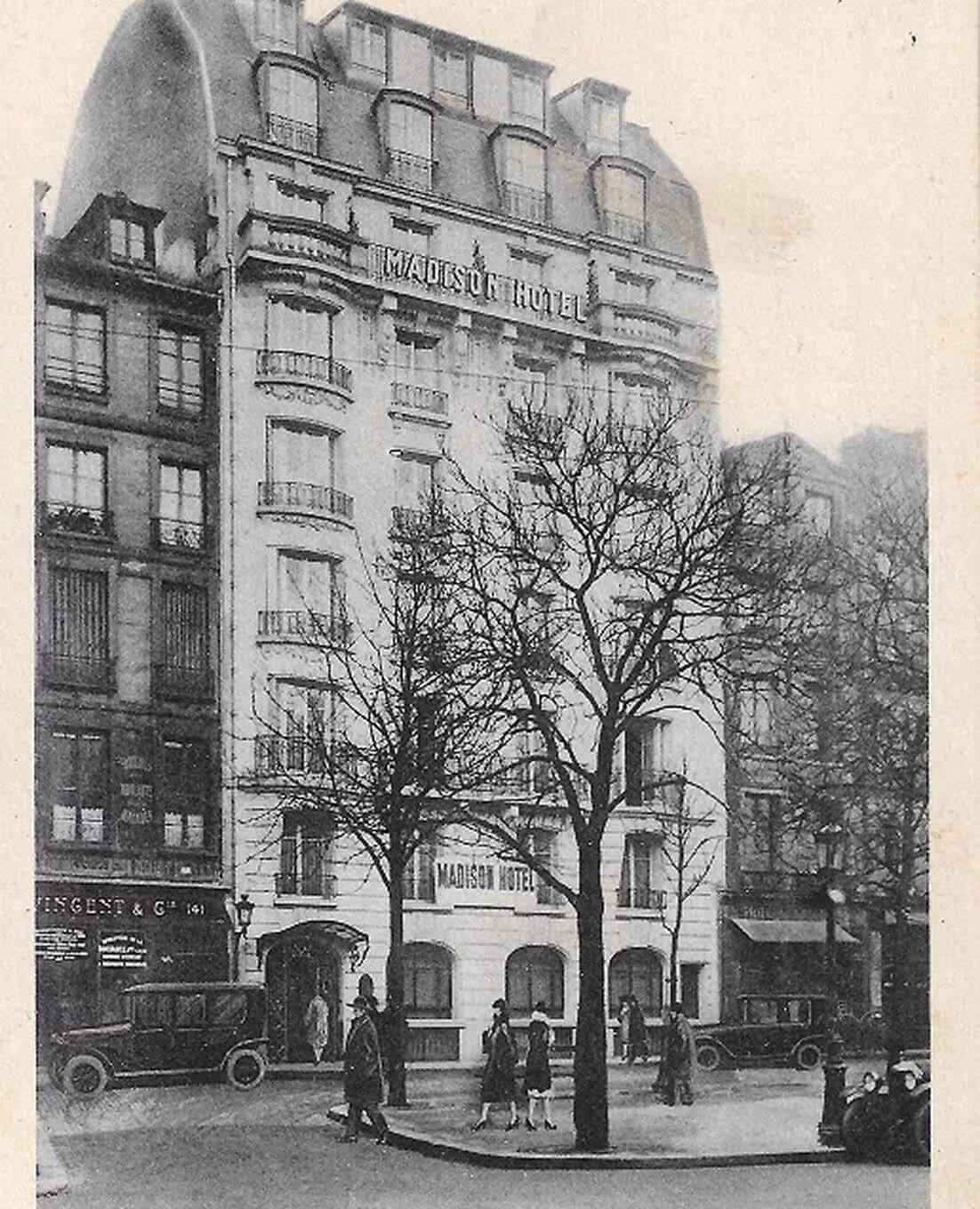 Façade classique de l'hôtel Madison avec voitures anciennes et passants dans une rue bordée d'arbres sans feuilles. - Hôtel Madison