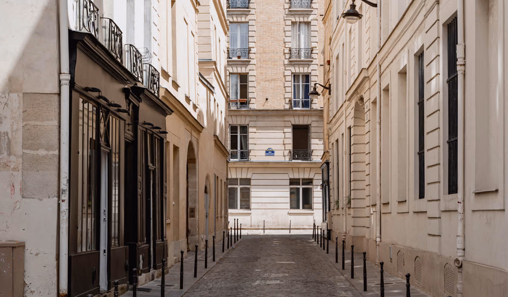 Ruelle pavée à Paris bordée de bâtiments résidentiels en pierre claire avec balcons en fer forgé. - Hôtel Madison