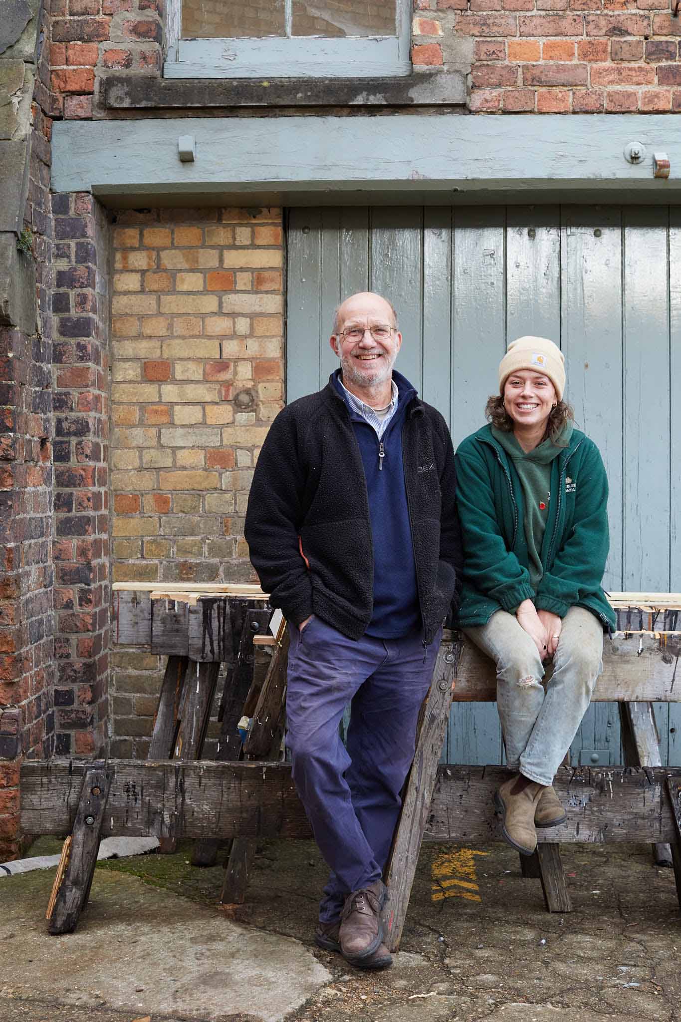 T Nielsen and Co man standing and woman sitting both smiling in front of red brick wall