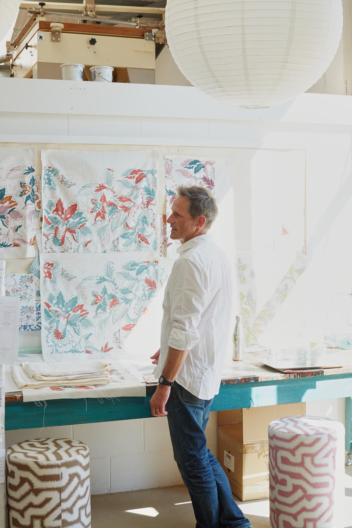 Rapture and Wright man standing in bright room looking at fabric on the wall footstools in front of wall