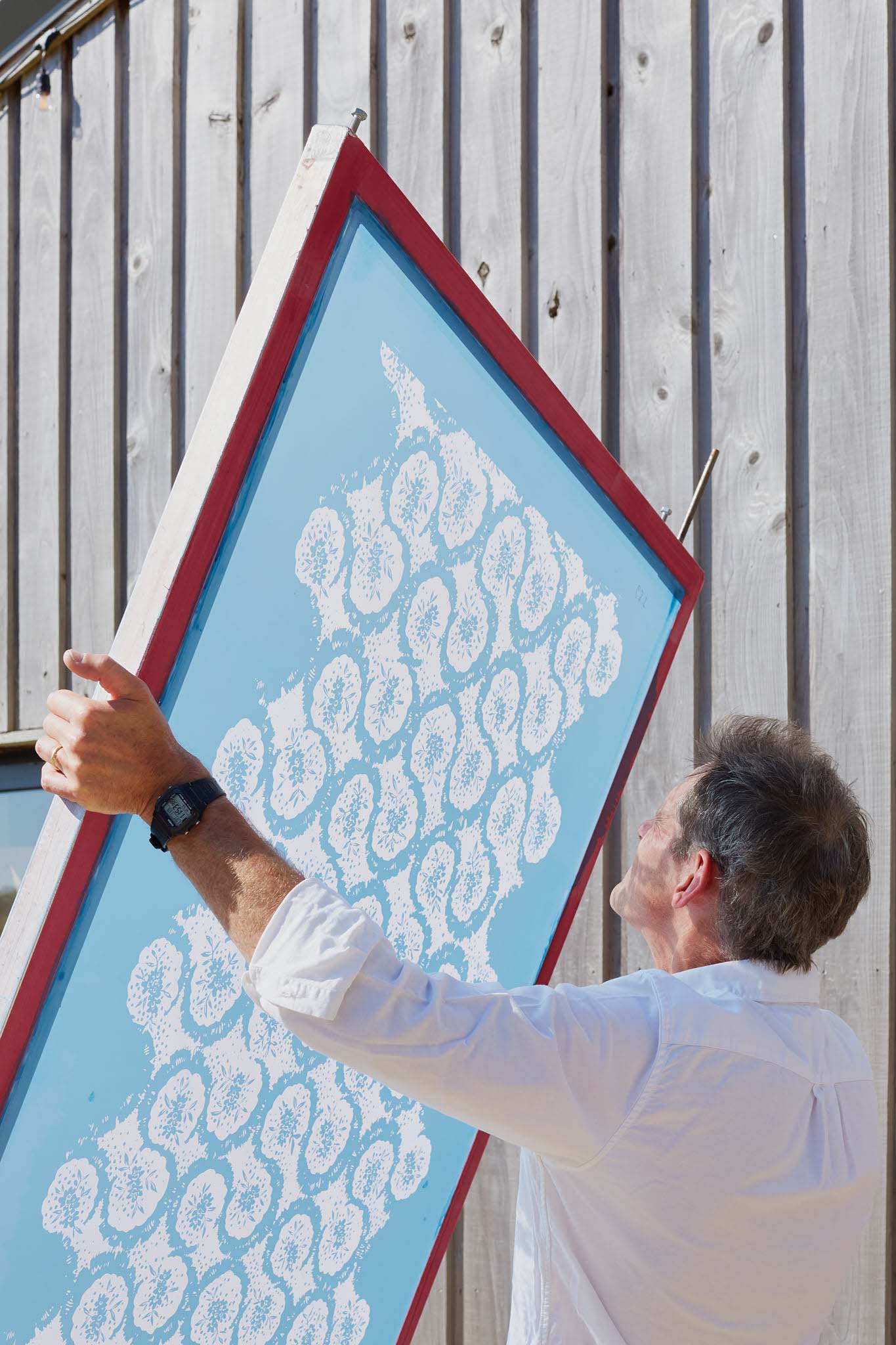 Rapture and Wright man holding silk screen print up to sky outside factory building  