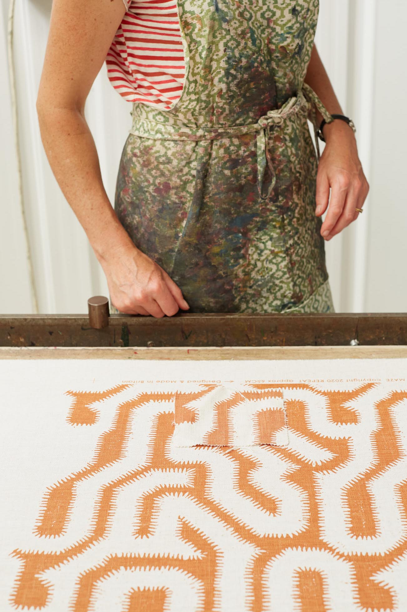 Rapture and Wright woman in apron standing in front of patterned fabric burn orange colour