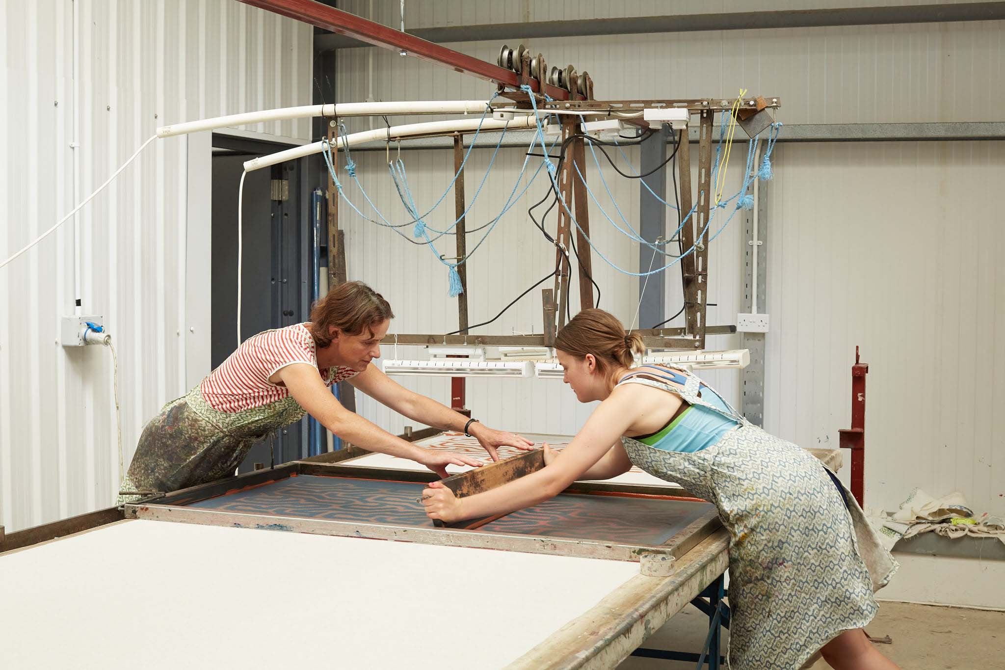 Rapture and Wright two woman working at silk screen printing table machine