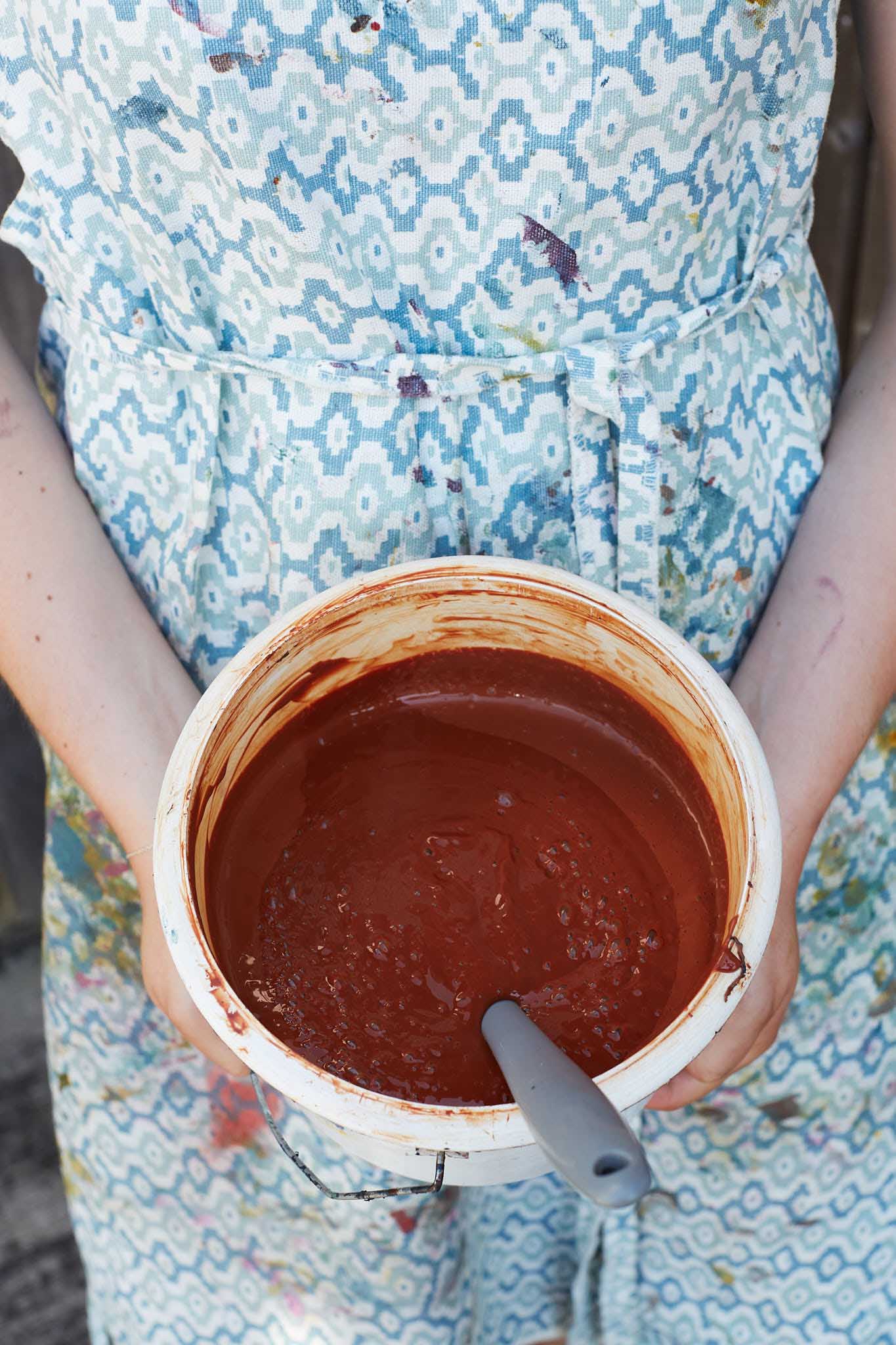 Rapture and Wright woman in apron dress holding pot of burnt orange colour dye paint